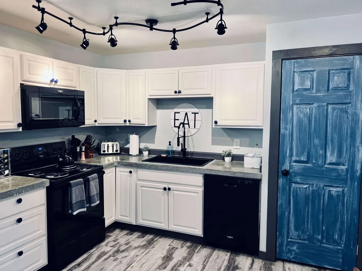 This image showcases a modern kitchen with black appliances, white cabinetry, and a decorative wall art displaying the word 'EAT'. The blue door adds a pop of color, while the countertop space appears ample for meal prep. The overall setting is inviting, bright, and functional, clearly depicting essential kitchen amenities.