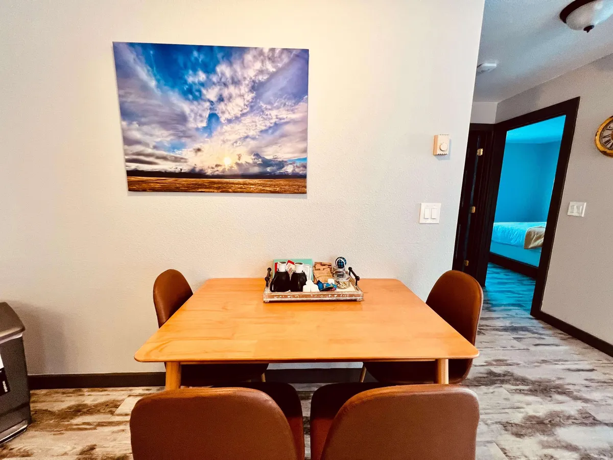 A cozy dining nook featuring a wooden table surrounded by comfortable brown chairs and accentuated with wall art depicting a dramatic sky. The setup feels warm and inviting, suitable for both shared meals and activities like board games or planning adventures.