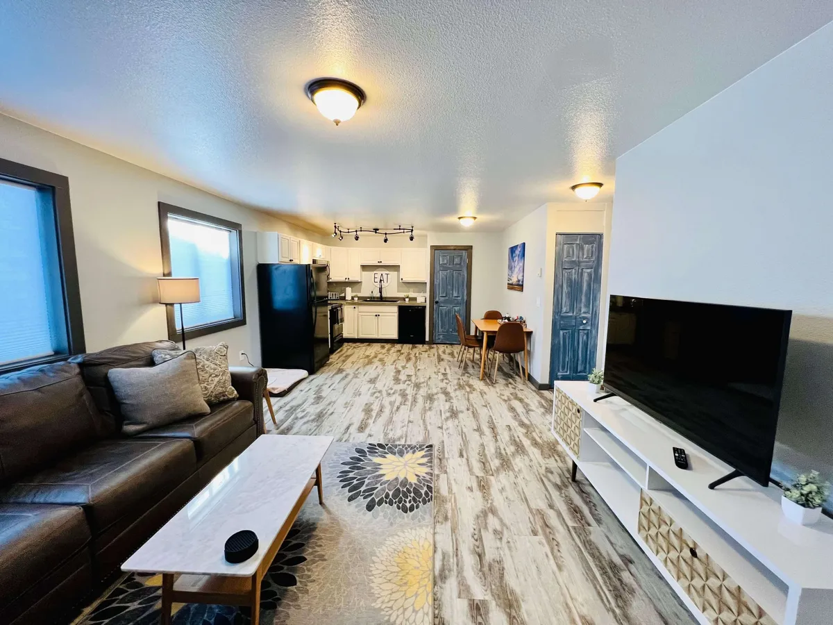 An open-concept living and dining area with a leather sofa, coffee table, TV unit, and a dining table in view. The layout emphasizes the seamless connection between the lounging and dining spaces, perfect for both unwinding and entertaining guests.